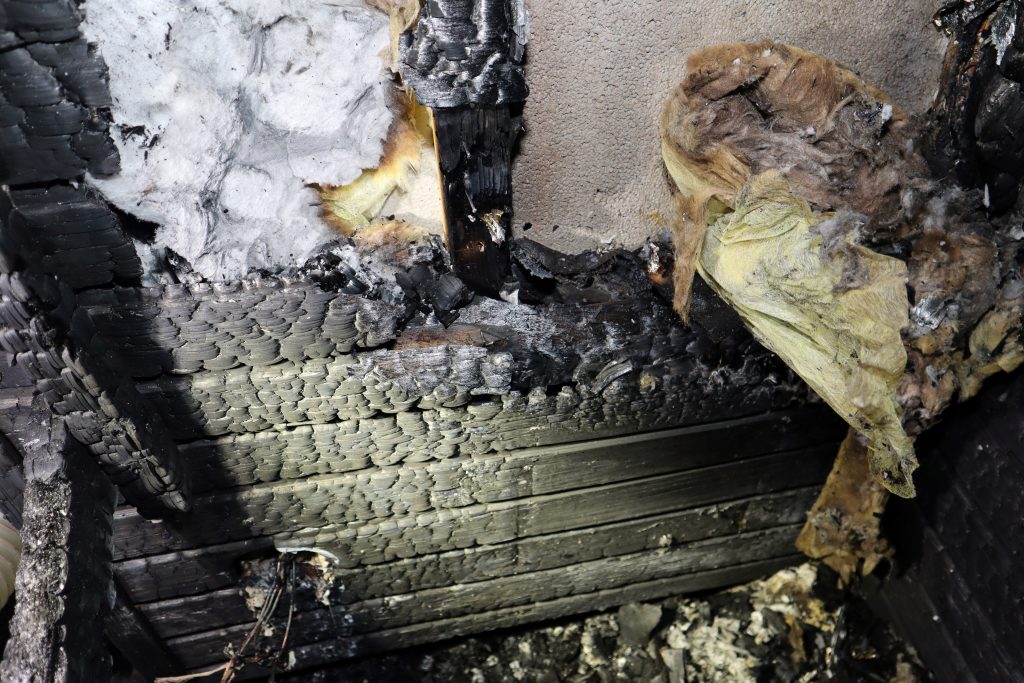 Palanut seinä kiukaan takana. Osa seinän eristemateriaalista on palajastunut puupaneloinnin takaa.